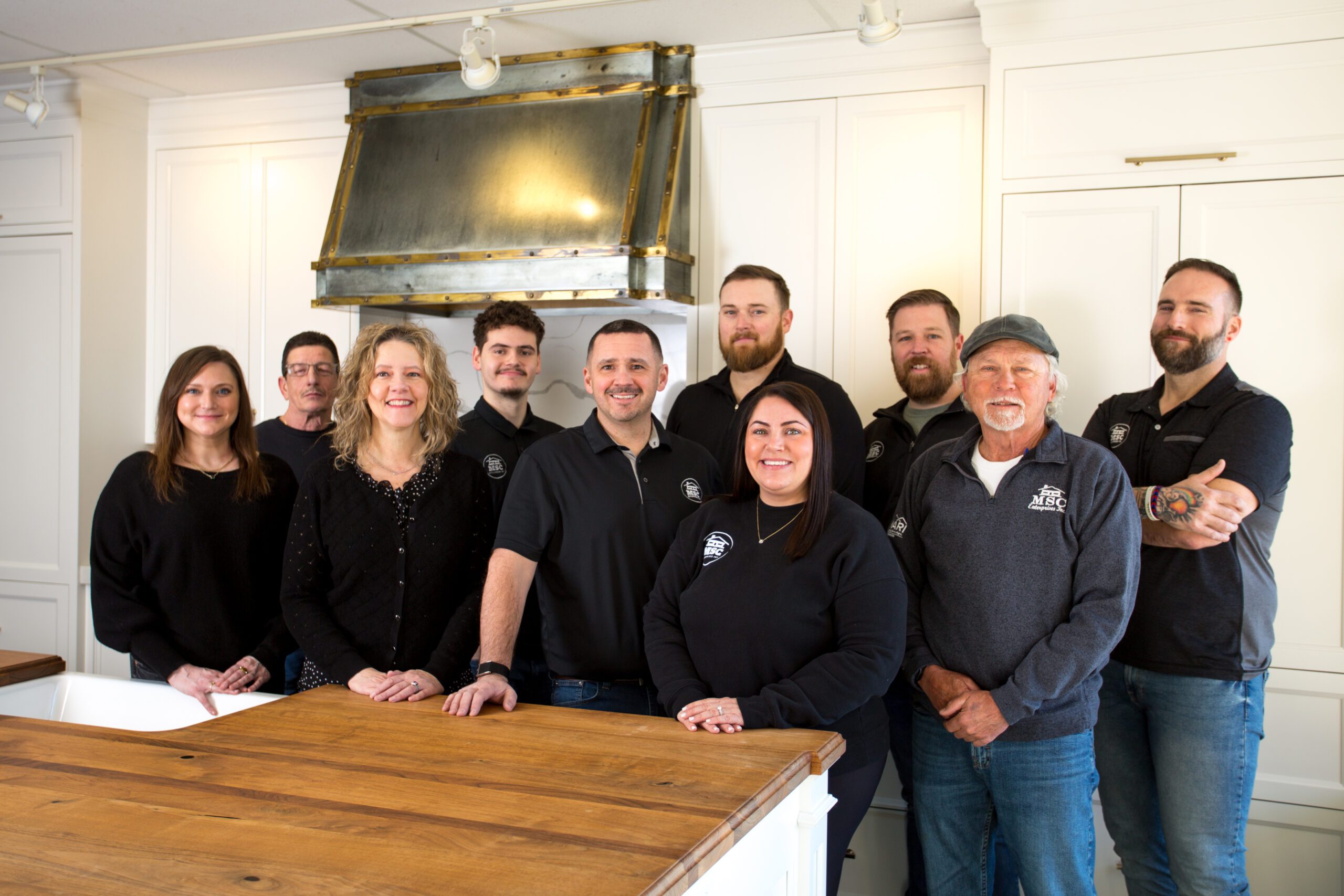 Team of MSC Enterprises, a family-owned remodeling contractor in Kansas City, standing in a kitchen setting with a wooden countertop, showcasing their commitment to quality craftsmanship and customer service.