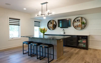 Modern basement bar with sleek cabinetry, statement lighting, and stone surfaces, featuring an island with seating, surrounded by open sightlines to lounge and game areas, emphasizing functionality and style in a Kansas City renovation.
