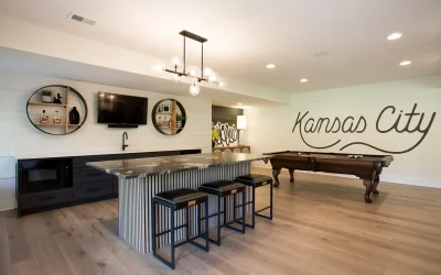 Modern basement bar and gathering island in Kansas City, featuring matte cabinetry, statement lighting, and stone surfaces, with a pool table and decorative wall art.