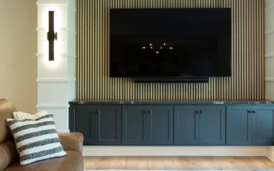 Modern basement lounge area featuring a dark cabinetry unit with a large flat-screen TV, accentuated by stylish wall lighting and textured paneling, designed for comfort and entertainment in a cohesive living space.