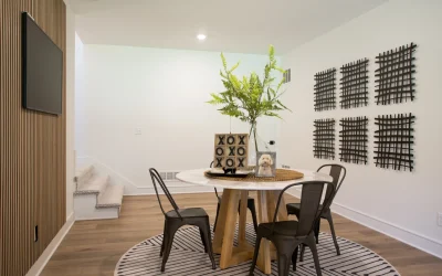 Modern basement gathering area with round table, black metal chairs, decorative plant centerpiece, textured wall art, and warm wood accents, reflecting functional and stylish design for entertaining.